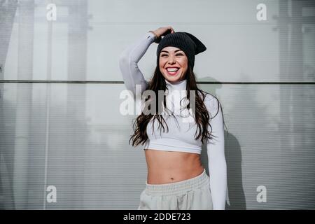 Happy woman wearing knit hat while standing against wall Stock Photo