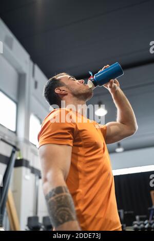 Thirsty man drinking water while standing in gym Stock Photo