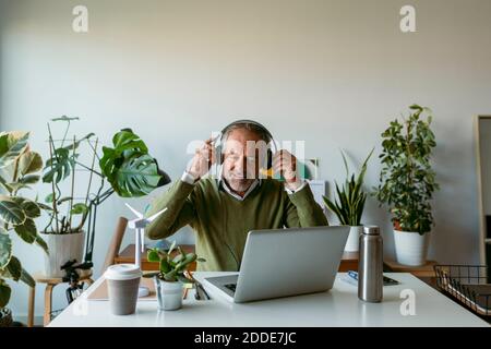 Smiling man wearing headphones while working on laptop at home Stock Photo
