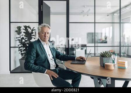 Senior man wearing suit using laptop while sitting on chair at office Stock Photo