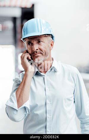 Male engineer in hardhat looking away while talking on smart phone in industry Stock Photo