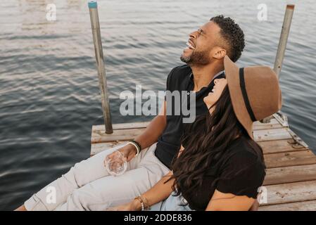 Happy couple drinking wine while sitting on pier Stock Photo