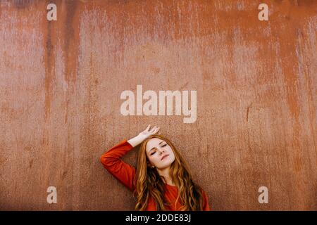 Young woman with eyes closed leaning on brown wall