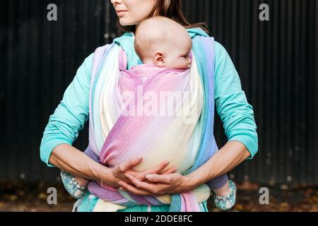 Midsection mother carrying baby wrapped in blanket standing against metal wall Stock Photo