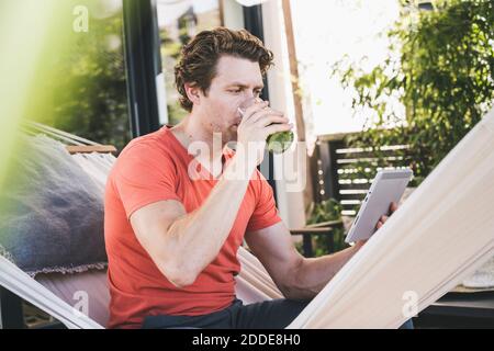 Mid adult man using digital tablet drinking juice while sitting at home Stock Photo