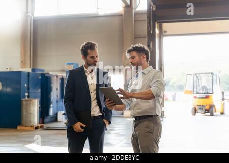 Mature man using digital tablet while discussing with businessman at factory Stock Photo