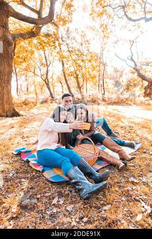 Family taking selfie on smart phone while sitting in park during autumn Stock Photo