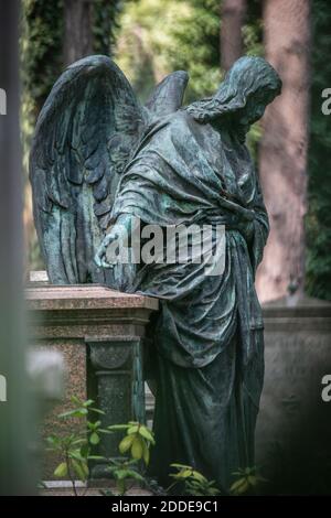 Weathered statue of angel standing beside tomb in cemetery Stock Photo