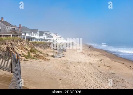 Woman walking along a sandy beach lined with holiday homes on a misty autumn morning Stock Photo