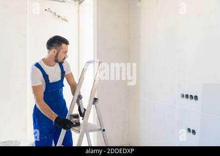 A handyman in overalls marks the wall using a laser level Stock Photo