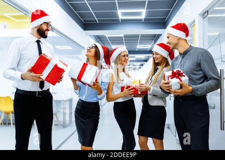 group of joyful colleagues in Santa Claus hats, with Christmas gifts, having fun and celebrating the New Year Stock Photo