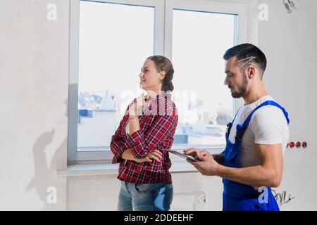 A architect in a blue overalls shows the client the renovation of an apartment. He writes notes with a pen Stock Photo