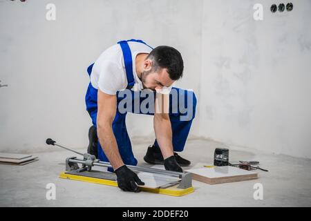 Young construction worker cuts tiles with a special tool Stock Photo