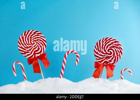 Christmas red candy canes and lollipops in snow on blue background. Merry Christmas sweets and Happy New Year concept Stock Photo