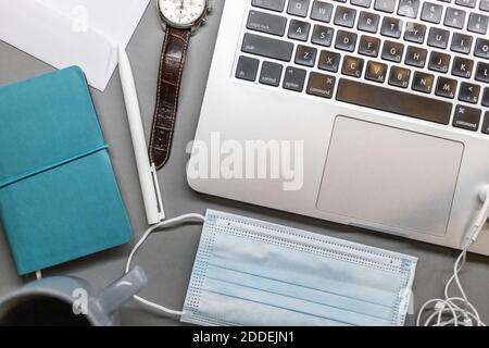 notebook laptop face mask watch and pen on grey table Stock Photo