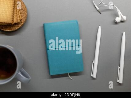 blue notebook cup cookie and pens on grey table Stock Photo