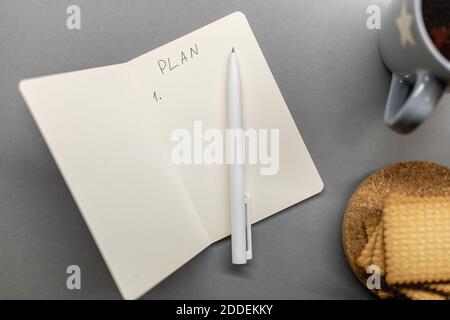 open notebook cup cookie and pen on grey table Stock Photo
