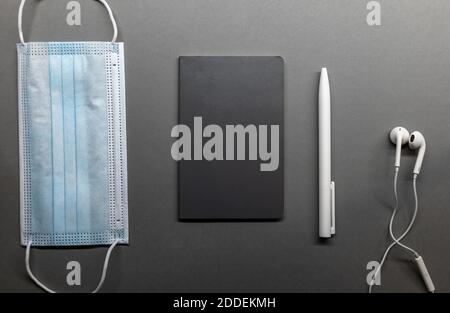grey notebook face mask and white pen on table flat lay Stock Photo