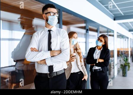 Business colleagues, office workers wearing medical protective masks on their faces chatting during coffee break, coronavirus, quarantine Stock Photo