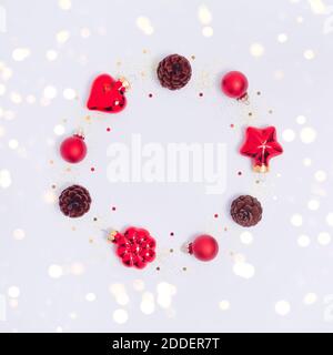 Christmas wreath made of red decorations, pine cones, confetti and glitter on white background. Round frame with lights. Flay lay with copy space Stock Photo
