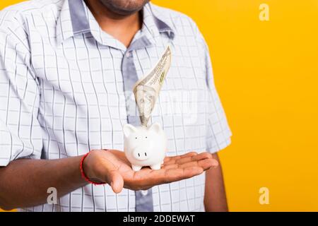 Asian happy portrait young business black man putting dollar bill banknote into a piggy bank, studio shot isolated on white background, Saving deposit Stock Photo