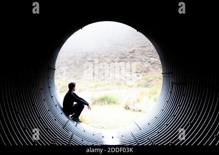 Silhouette of a man looking pensively at the edge of a tunnel through the mist of the mountain Stock Photo
