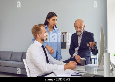 Serious experienced manager pointing at mistake on computer screen while talking to his employees Stock Photo