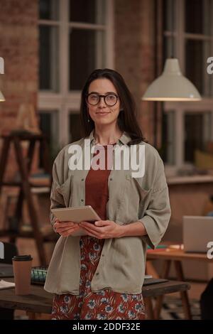 Portrait of young businesswoman in eyeglasses with tablet pc smiling at camera at office Stock Photo