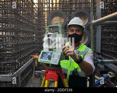 Land surveyor dressed in hardhat,mask and protective vest works on total station Stock Photo