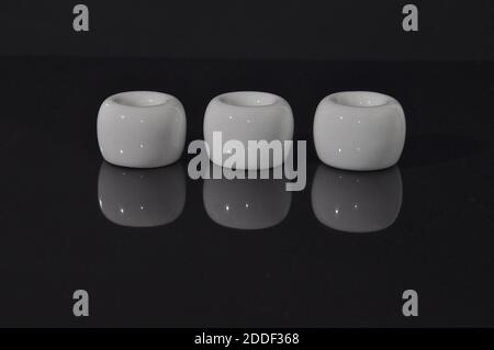 A row of white ceramic cylinders on a shiny black reflective surface, showing an inverted mirror image. Stock Photo