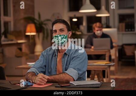 Portrait of young office worker in protective mask working at his workplace at modern office Stock Photo