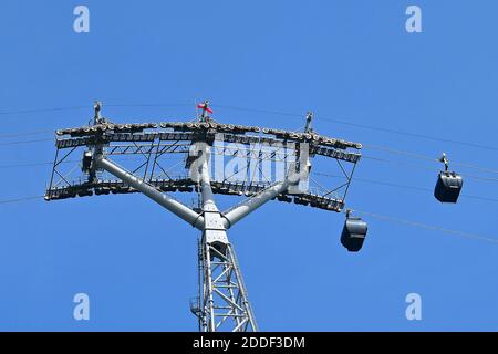 An upward perspective view of cable cars and supporting pylon against a bright blue sky background. Stock Photo