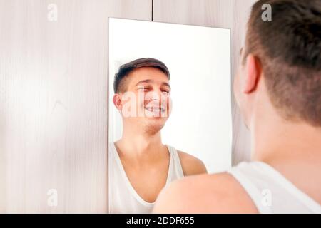 Happy Young Man looking to Reflection in the Mirror at the Home Stock Photo