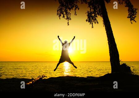 Toned Photo of Happy Person jump on the Sunset Background at Seaside Stock Photo