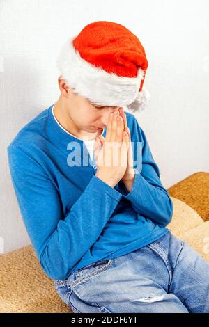 Young Man in Santa Hat is Praying by the White Wall in the Room Stock Photo