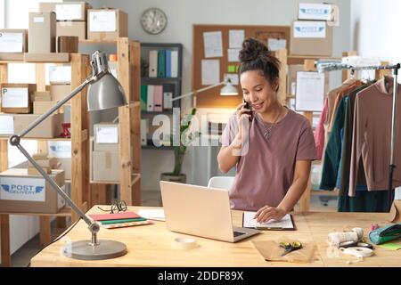 Female tailor using laptop and talking on the phone during her work in workshop Stock Photo