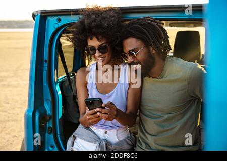 Beautiful couple sitting at the back of car and using smart phones Stock Photo