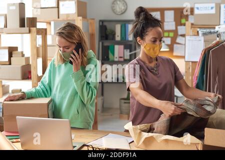 Young two women in protective masks packing clothes into the boxes working in delivery service Stock Photo