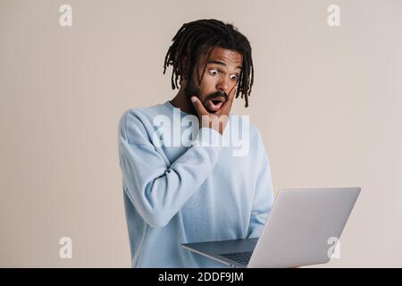 Shocked african american guy holding and looking at laptop isolated over white background Stock Photo