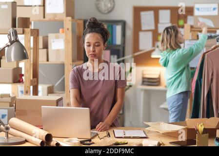 Young serious woman standing near her workplace and using laptop at work during working day in workshop Stock Photo