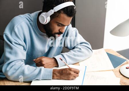 Confident young african man studying at the desk, wearing wireless headphones Stock Photo