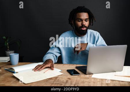 Handsome young african man sitting at a coffee shop with pensive look, thinking of business plans, working on laptop Stock Photo