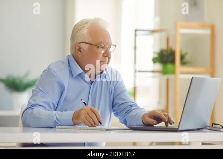 Senior man using laptop and writing in notebook, studying new information or managing budget Stock Photo