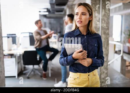 Business woman with a tablet, her co-workers discussing business matters in the background Stock Photo
