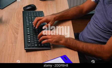 Close up of man's hands typing on keyboard sitting on chair in front of computer. Busy entrepreneur in new normal office workplace corporate writing on computer keyboard looking at desktop Stock Photo