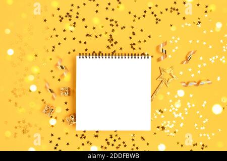 Notepad mockup with magic wand and gift boxes on a yellow glittering background. Golden shiny confetti. Stock Photo