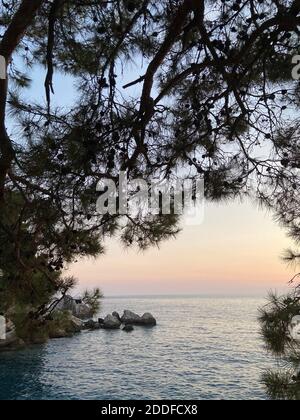 Beautiful romantic sunset on the Aegean Sea with pine trees and hills on the horizon. Reflections of the dawn over the sea. Dramatic colors of skies. Stock Photo