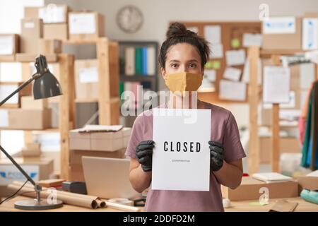 Portrait of young woman in protective mask holding placard in her hands while standing at office Stock Photo