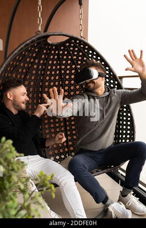 young man with VR goggles sitting on the swing with his friend. Developers testing virtual reality glasses. . High quality photo Stock Photo