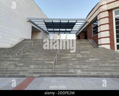 Concrete stone walls and stairs with steel rails, modern architecture building with red bricks, glass shade, cat sitting on the empty stairway. Stock Photo